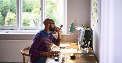 Person working from home at a desk with desktop computer and notes on wall, reflecting LGRA's flexible work culture