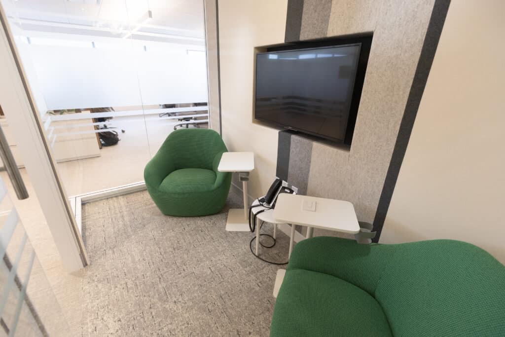 Small LGRA huddle room with green chairs, wall-mounted screen, and glass walls