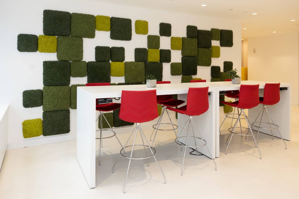 Modern collaborative workspace with red chairs, white tables, and green moss wall decor in LGRA office